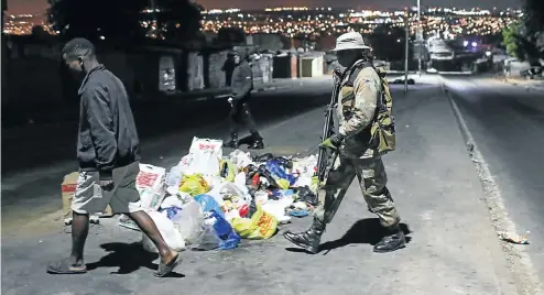  ?? Pictures: Alaister Russell ?? A member of the South African National Defence Force on patrol in Alexandra township, Johannesbu­rg, ushers a curfew-breaker home this week.