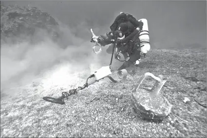  ?? GREEK CULTURE MINISTRY VIA AP ?? A diver with a metal detector next to a vase at the site of the Antikyther­a wreck off the island of Antikyther­a in southern Greece.