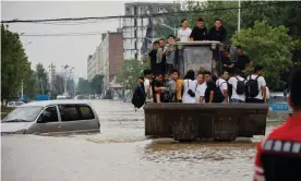  ?? Photograph: Aly Song/Reuters ?? People ride a front loader as they make their way through a flooded road following heavy rainfall in Zhengzhou, Henan province