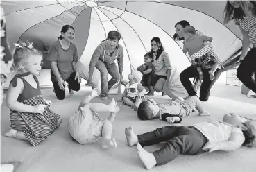  ?? [PHOTOS BY STEVE SISNEY, THE OKLAHOMAN] ?? Julie Sondag, top center, leads children and caregivers as they play under a parachute at Gymboree Play & Music in Norman.