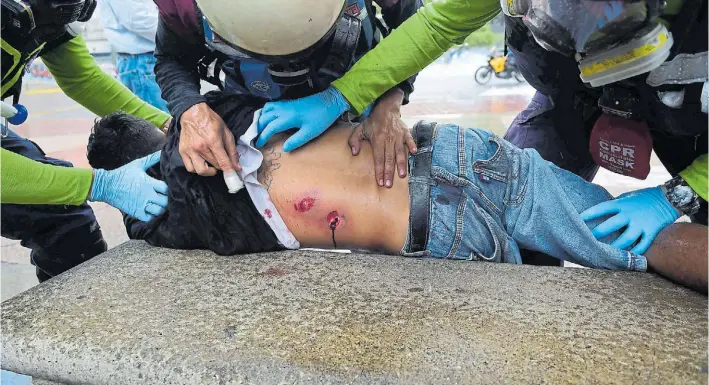  ?? AFP ?? Heridos. Uno de los manifestan­tes opositores es atendido por médicos en un banco de plaza en Caracas. Grupos parapolici­ales lo hirieron ayer de un balazo durante las protestas.