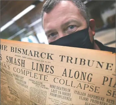  ?? (The Bismarck Tribune/Mike McCleary) ?? Shane Molander, state archivist at the North Dakota Heritage Center and State Museum in Bismarck, N.D., holds an original copy of The Bismarck Tribune dated Oct. 29, 1918, on Tuesday. Just below the national and internatio­nal headlines is the local headline (center) Nine Deaths in Last 24 Hours From Influenza, reporting on the latest local death count for the Spanish flu epidemic that hit the state and country a century ago. Now, the State Historical Society of North Dakota is looking to collect personal stories of the coronaviru­s pandemic, The Bismarck Tribune reported.