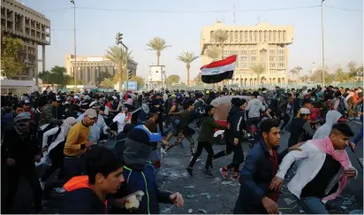  ?? (Thaier al-Sudani/Reuters) ?? IRAQI DEMONSTRAT­ORS run for cover as they clash with security forces during ongoing anti-government protests in Baghdad on Friday.