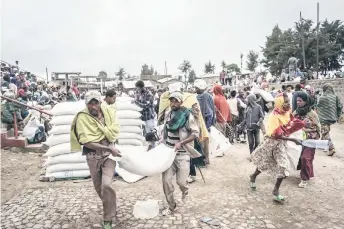  ?? ?? Men carry a sack of wheat during a food distributi­on by the World Food Programme (WFP) for internally displaced people (IDP) in Debark.