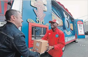  ?? ELAINE THOMPSON THE ASSOCIATED PRESS ?? Amazon worker Khayyam Kain, right, hands off a package to a customer at an Amazon Treasure Truck in Seattle. The Treasure Truck is a quirky way for the online retailer to connect with shoppers in person.