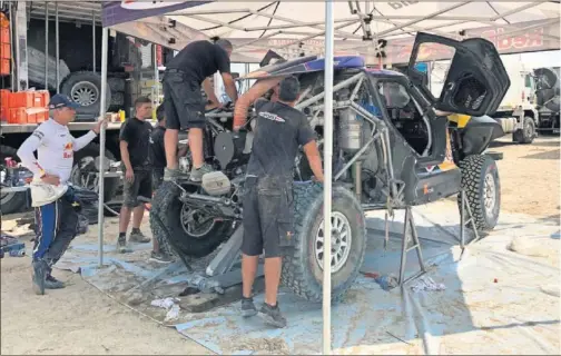  ??  ?? Carlos Sainz observa como trabajan los mecánicos para reparar las averías que sufrió su Mini en la novena etapa del Dakar 2019 .