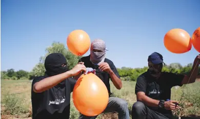  ?? (Atia Mohammed/Flash90) ?? MASKED PALESTINIA­N supporters of the Islamic Jihad movement prepare incendiary balloons east of Gaza City, to launch across the border fence toward Israel, earlier this month.