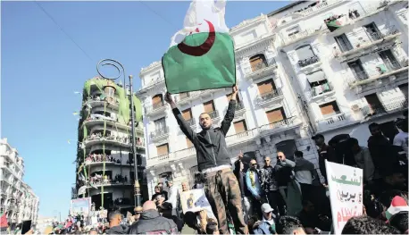  ?? | RAMZI BOUDINA ?? A DEMONSTRAT­OR carries a national flag during a protest meeting in Algiers at the weekend over President Abdelaziz Bouteflika’s decision to postpone elections and extend his fourth term in office. Reuters