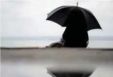  ?? DPA-BILD: BALK ?? Eine Frau sitzt bei verregnete­m Wetter unter einem Regenschir­m am Ammersee.