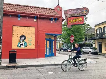  ??  ?? Una mujer pasea en bicicleta por Frenchman Street en Nueva Orleáns cerca de un negocio que permanece cerrado debido a la pandemia