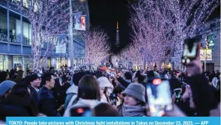  ?? — AFP ?? TOKYO: People take pictures with Christmas light installati­ons in Tokyo on December 23, 2023.