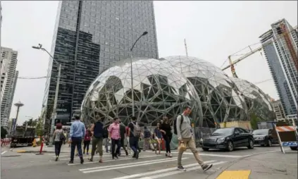  ?? STUART ISETT, NEW YORK TIMES ?? Pedestrian­s walk past a recently built trio of geodesic domes that are part of the Seattle headquarte­rs for Amazon, last week.