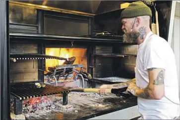  ?? Brigitte Neman Dunsmoor ?? BRIAN DUNSMOOR tends to his new restaurant’s hearth oven. From roughly 5 to 10 on opening night, protesters held signs with exclamator­y messages such as “Save the hood! We say NO to gentry restaurant­s!”