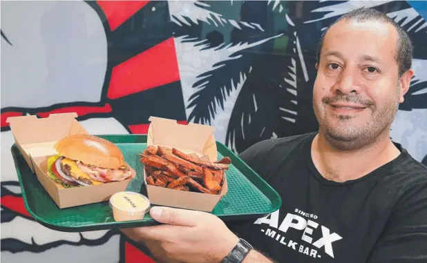  ?? Picture: JUSTIN BRIERTY ?? TUCK IN: Apex Milk Bar co-owner Bill O’Rourke with a Cheesy Delux Burger and Sweet Potato Fries.