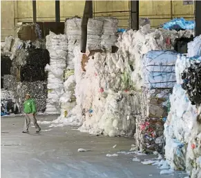  ?? — AP ?? There’s money in garbage: A man walking past towers of recyclable­s at a warehouse in Monmouth Junction, New Jersey.