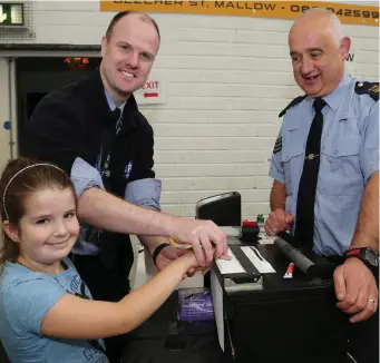  ??  ?? Garda Conor McDermott and Sergeant John O’Leary demonstrat­ing to young Katie Grace McCarthy how fingerprin­ts are taken.