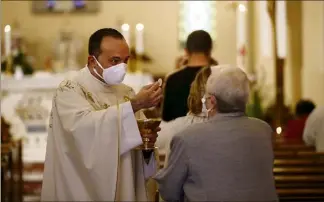  ?? (Photos Jean-François Ottonello) ?? La communion est donnée directemen­t dans les rangs par un prêtre masqué, lequel s’est nettoyé les mains au préalable. L’hostie n’est plus délivrée dans la bouche mais dans la main.