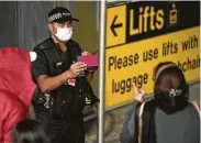  ?? Oli Scarff / AFP via Getty Images ?? A police officer talks to passengers at Manchester Airport on Monday, the first day of a 14-day quarantine on travelers coming into England.