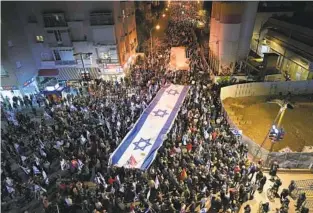  ?? TSAFRIR ABAYOV AP PHOTOS ?? Israelis march with a large banner featuring the national flag during a protest Saturday in Tel Aviv against plans by the new government to overhaul the judicial system.