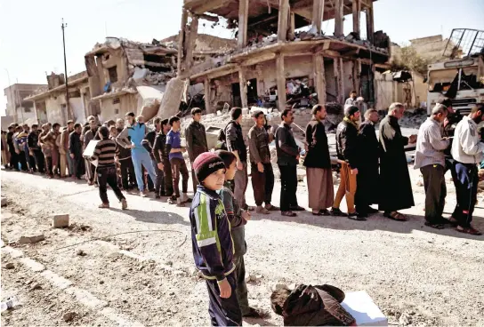  ??  ?? People line up during a food distributi­on by Iraqi forces in west Mosul as Iraqi forces advance in the city in the ongoing battle to seize it from Daesh. (AFP)