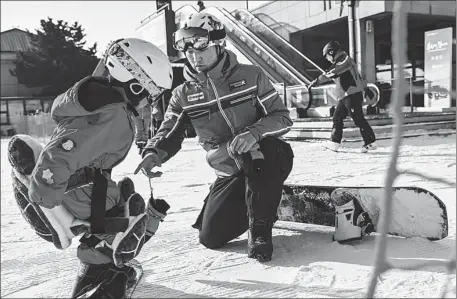  ?? PENG ZIYANG / XINHUA ?? Zhu Yunpeng, a snow sports coach, teaches a child how to snowboard at Vanke Shijinglon­g Ski Resort in Beijing’s Yanqing district on Dec 14.