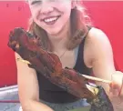  ?? GRACE MCDERMOTT / MILWAUKEE JOURNAL SENTINEL ?? Rachel Ryan, a Milwaukee Journal Sentinel intern, holds up a Gator Claw On-A-Stick at the 2021 Wisconsin State Fair. This grilled alligator arm served with the claw still attached is available at Exotic Meat Grill.