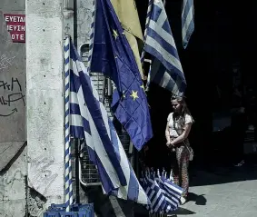  ??  ?? In vendita Una ragazza in strada vicino alle bandiere dell’Ue e della Grecia (Afp)