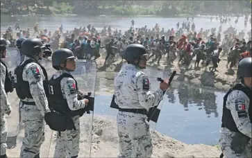  ?? Marco Ugarte Associated Press ?? MEXICAN troops stand on the banks of the Suchiate River where Central American migrants are crossing from Guatemala. Mexico’s strategy is to break up masses of people into smaller groups to prevent caravans.