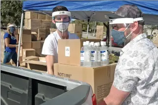  ?? Dan Watson/The Signal ?? (Above) Peter Warda, left, and Ivan Volschenk load a truck with masks, face shields and hand sanitizer from the Santa Clarita Valley Chamber of Commerce pick-up site during the PPE United driveup event, held Saturday in the Westfield Valencia Town Center parking lot. (Below) SCV Chamber board member Becki Robb stacks boxes of face masks during the pick-up event.