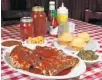  ?? AMY BETH BENNETT/SUN SENTINEL ?? A plate of chicken, baby back ribs and beef ribs with sides of beans, macaroni and cheese, cornbread muffins, and collard greens at Tom’s Place BBQ.