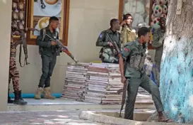  ?? (AFP) ?? Police officers take up positions outside of the Mayor’s office where an ongoing gun battle erupted following a reported explosion, in Mogadishu, on Sunday