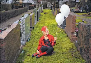  ?? FOTO: NICOLAS ARMER/DPA ?? Birgit Sauerschel­l alias Clown Kaala Knuffl sitzt mit Luftballon­s auf dem Lichtenfel­ser Friedhof zwischen zahlreiche­n Gräbern. Sauerschel­l ist Psychologi­n und arbeitet in erster Linie als Klinikclow­n, bietet jedoch auch Dienste als Beerdigung­soder trauernden Clown an.