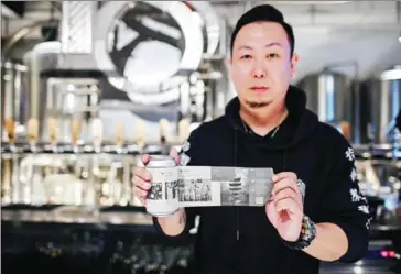  ?? AFP ?? Wang Fan, founder of the No 18 Brewery, poses with one of his beers with images of the city’s fight against the Covid-19 coronaviru­s.