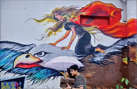  ?? REUTERS ?? People walk past a graffiti-painted wall during a rain shower in New Delhi on Saturday.