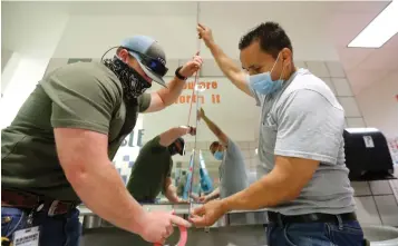  ?? Associated Press ?? ■ Wearing masks amid the concern of COVID-19, Richardson Independen­t School District workers Rogelio Ponciano, right, and Matt Attaway install a plexiglass barrier on the sink in the restroom Wednesday for students at Bukhair Elementary School in Dallas.