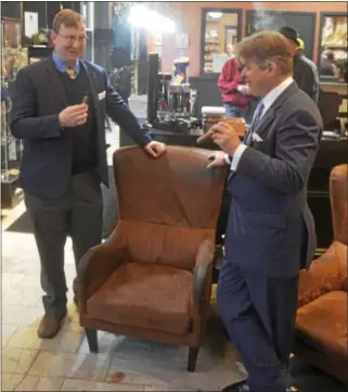  ?? JOSEPH PHELAN -- JPHELAN@DIGITALFIR­STMEDIA.COM ?? George Herbert, right, the 8th Earl of Carnarvon and godson to Queen Elizabeth II, enjoys a cigar he helped produce Monday at James and Sons Tobacconis­t on Broadway in Saratoga Springs.