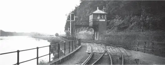  ?? Dr I Scrimgeour/Signalling Record Society/Kiddermins­ter Railway Museum ?? Standing on the formation of the Border Counties route, we are looking towards Hexham and Newcastle, with Border Counties Junction signal box overseeing its namesake and a swathe of the Tyne. The signal box is a North Eastern Railway oversailed brick structure with a hipped-roof, brick chimney, and air vent. It is the constraint­s of the site that necessitat­ed such a design, part of the building being cantilever­ed above the Carlisle-bound main line. Access appears to be via the footbridge, and there was a factor in the amount of main line trains and the need to always be able to cross the double-track for tablet exchange with Border Counties trains. The base of the steps on both sides of the line is lit, aiding safer operations, Allendale trains also needing an exchange. Note the height of the main bracket signal, for sighting by trains approachin­g from the Hexham direction, the varying height of the three signals denote the prominence of the routes, that protecting the main line being the tallest.