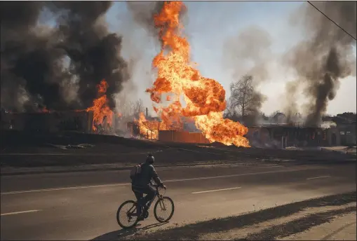  ?? (AP/Felipe Dana) ?? A man rides his bike March 25 past flames and smoke rising from a fire following a Russian attack in Kharkiv, Ukraine.