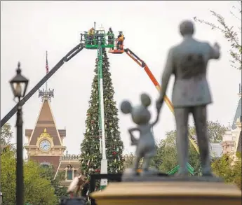  ?? Photograph­s by Allen J. Schaben Los Angeles Times ?? A CREW puts the finishing touches on a giant Christmas tree and other holiday decoration­s along Main Street U.S.A. as seen from behind the “Partners” statue of Walt Disney holding Mickey Mouse’s hand.