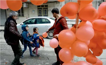  ?? AFP ?? A Syrian man hands a balloon to a girl in front of a shop selling Valentine’s day gifts in the town of Qamishli. —