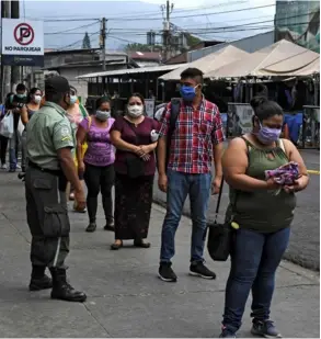  ?? AFP ?? Un policía resguarda el orden mientras estas personas esperan turno para entrar al mercado de Santa Tecla.
