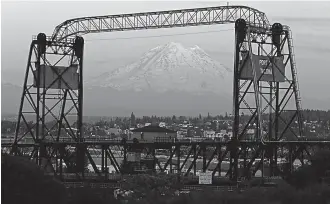  ?? AP Photo/Ted S. Warren ?? ■ In this Monday photo, Mount Rainier is seen at dusk and framed by the Murray Morgan Bridge in downtown Tacoma, Wash. The eruption of the Kilauea volcano in Hawaii has geological experts along the West Coast warily eyeing the volcanic peaks in...