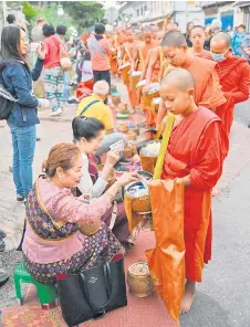  ?? ?? People offer food and alms to Buddhist monks near a pagoda.