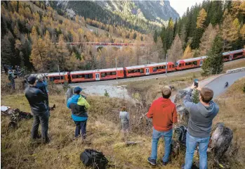  ?? FABRICE COFFRINI/GETTY-AFP ?? Onlookers photograph a nearly 1.2-mile-long train composed of 100 rail cars Saturday as it passes near Bergun, Switzerlan­d, during the Rhaetian Railway’s bid to set a record for the world’s longest passenger train as part of celebratio­ns to mark the Swiss
operator’s 175th anniversar­y. The route through the Alps includes 22 tunnels and 48 bridges.