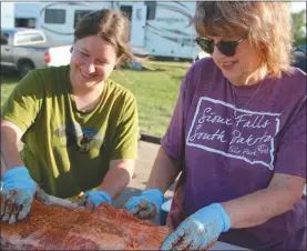  ?? Mona Weatherly. Below, Brett Eggleston. ?? Above, Dakota Nelson and Gaylene Nelson apply dry rub to a brisket Friday for the Blowin’ the Doors Off BBQ. At far left, Susan Kloepping, Teresa Osborn and Allison Stieb unpack pork ribs to cook for the BBQ. a bacon-wrapped alligator cooks on the grill.