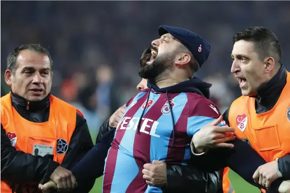  ?? EPA ?? A Trabzonspo­r supporter is escorted from the pitch amid violent scenes at the end of Sunday night’s Super Lig match against Fenerbahce