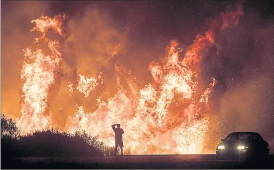  ?? THE ASSOCIATED PRESS ?? A motorist on Highway 101 watches flames from the Thomas fire leap above the roadway north of Ventura on Dec. 6, 2017. The largest wildfire recorded in California is officially out nearly six months after it began. Los Padres National Forest officials...