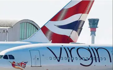  ?? Reuters ?? Back to Heathrow: A British airways aeroplane tailfin and a Virgin Atlantic aeroplane are seen with the control tower at Heathrow airport. Virgin Atlantic said it planned to cut 3,150 jobs and would move its flying programme from London Gatwick to Heathrow airport. —