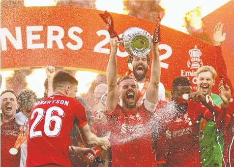  ?? HANNAH McKAY/REUTERS ?? Liverpool's Jordan Henderson lifts the trophy surrounded by celebratin­g teammates after winning the FA Cup 6-5 in a penalty shootout against Chelsea at Wembley Stadium in London on Saturday.