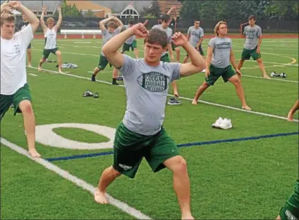  ?? JOHN KAMPF — THE NEWS-HERALD ?? Lake Catholic senior Bobby Williams, center, and members of the Cougars’ football team go through a 40-minute yoga session prior to practice Aug. 8.